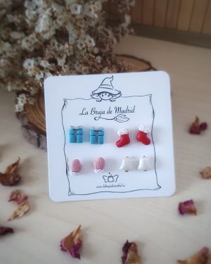 Se ve una tarjeta con 4 pares de mini pendientes de temática navidad. Paquete de regalo, calcetines, manoplas y campanas.