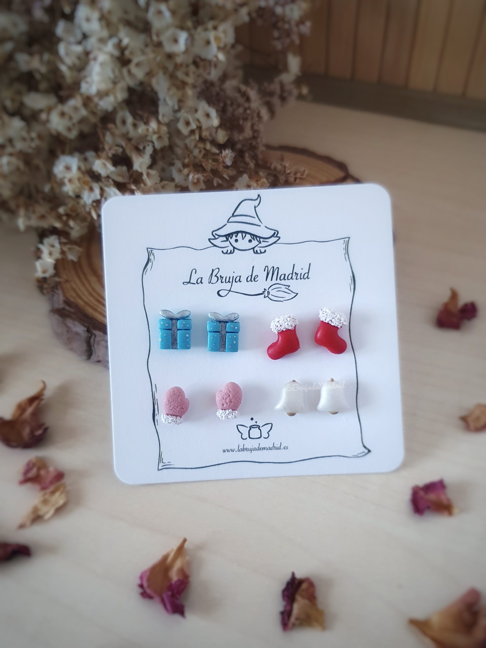 Se ve una tarjeta con 4 pares de mini pendientes de temática navidad. Paquete de regalo, calcetines, manoplas y campanas.