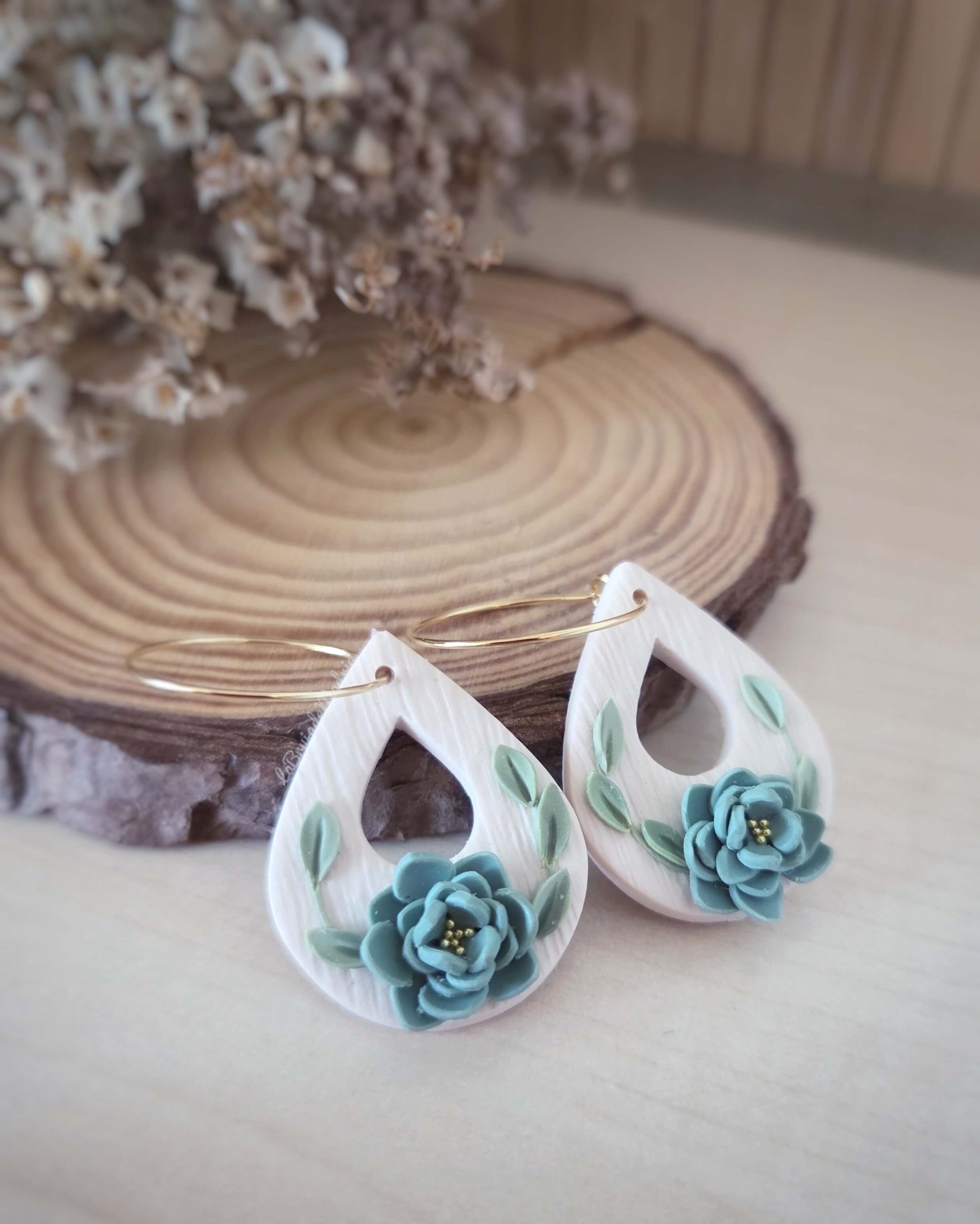 Pendientes Jade artesanales con aro dorado y flores verdes fotografiados sobre rodaja de madera