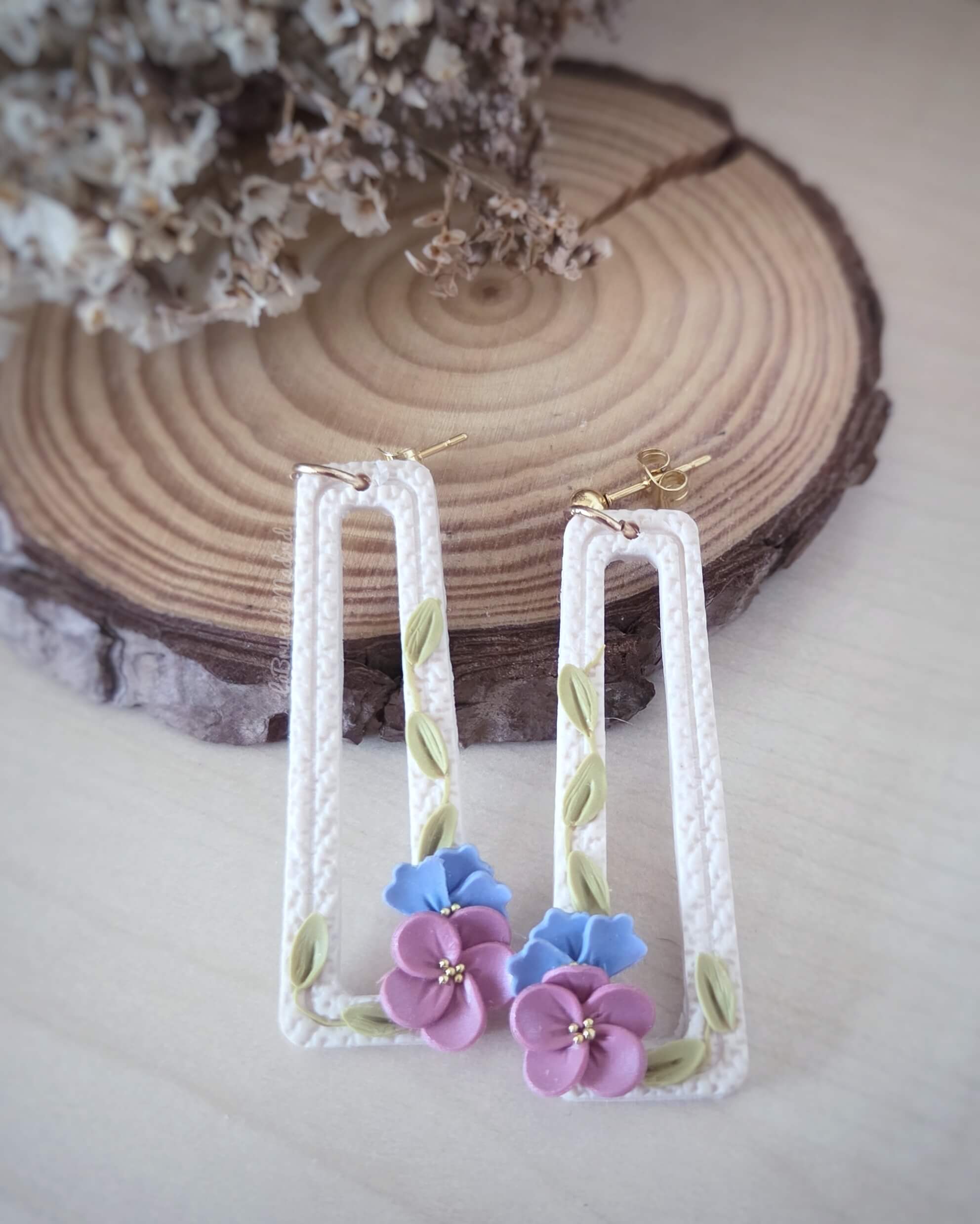 Detalle de flores malva y azul modeladas a mano en pendientes Pensamientos artesanales
