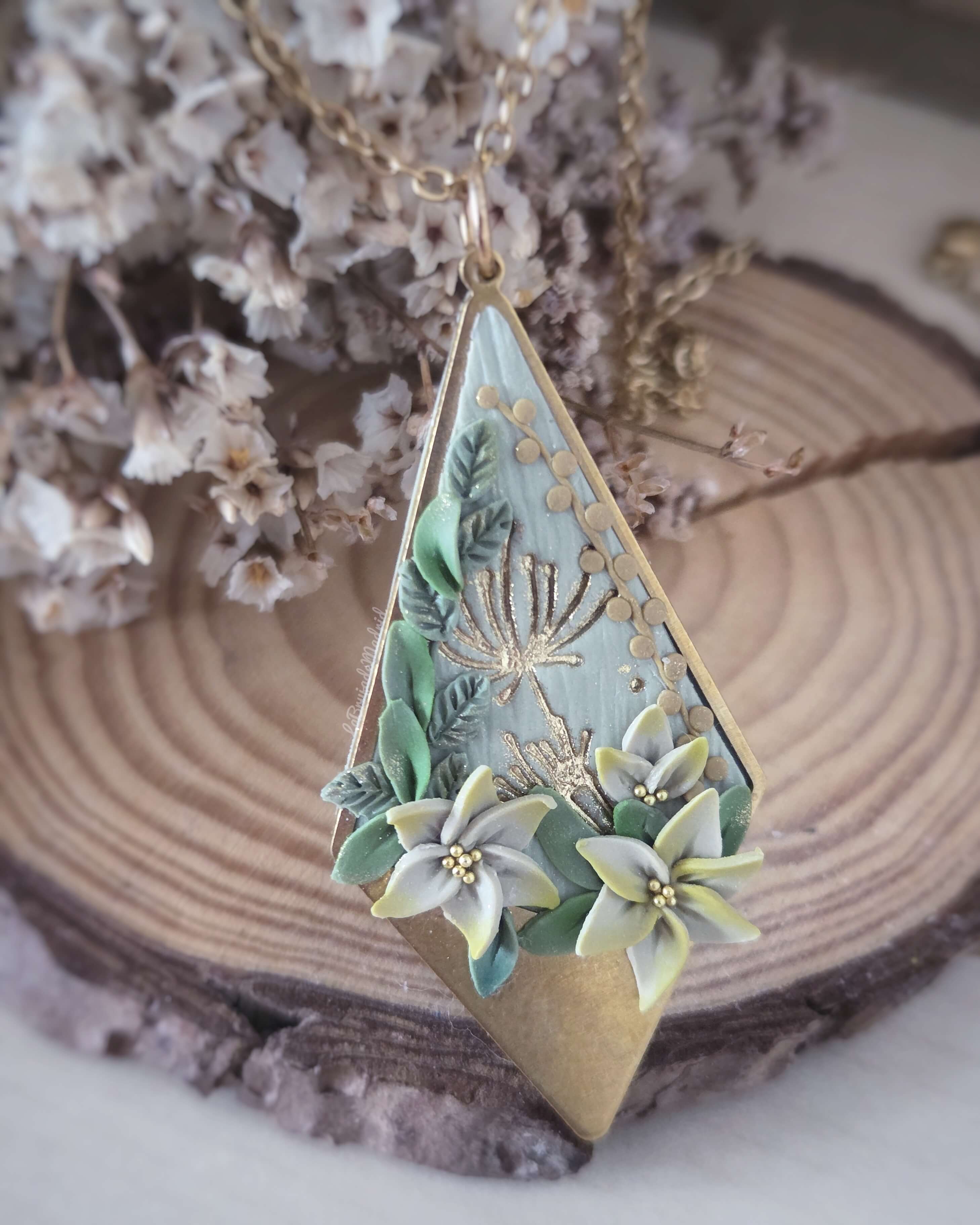 Colgante artesanal de arcilla polimérica inspirado en la paleta Botánica viva, decorado con flores rosas, hojas modeladas a mano y detalles dorados sobre base metálica.