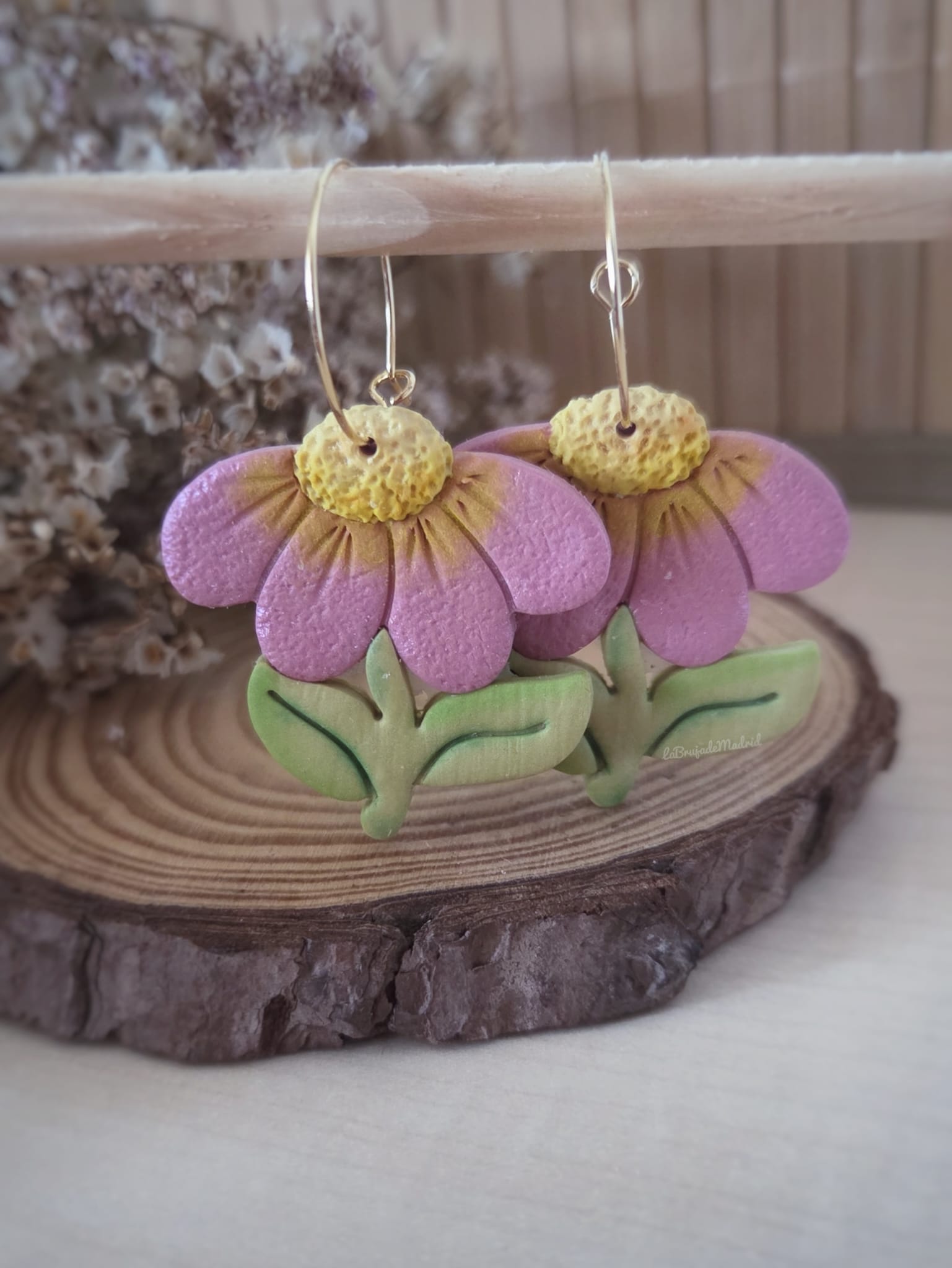 Pendientes artesanales de flor de equinácea en arcilla polimérica con pétalos rosas, centro amarillo y hojas verdes. Hechos a mano con arcilla polimerica y aros de acero inoxidable para orejitas sensibles.